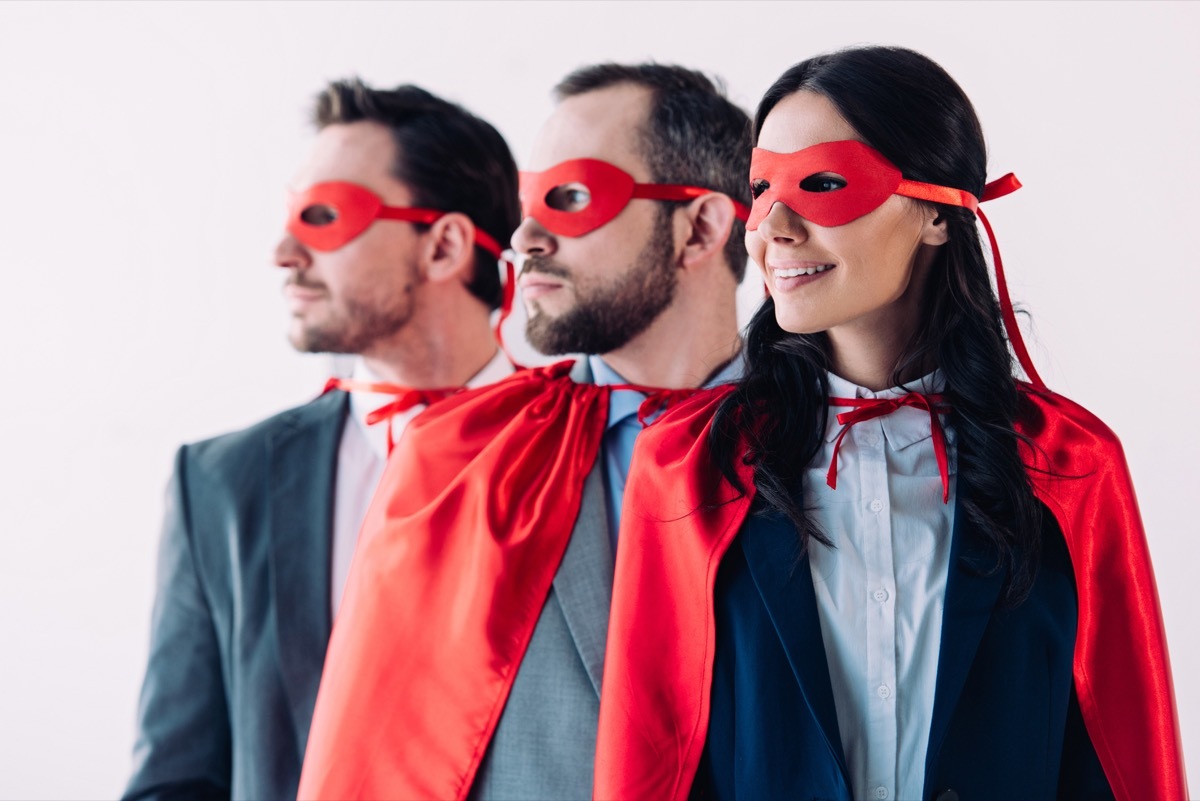 super businesspeople in masks and capes looking away in line in office - Image