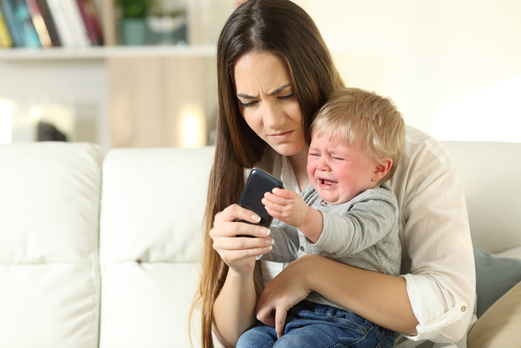 mom checks phone as toddler cries.