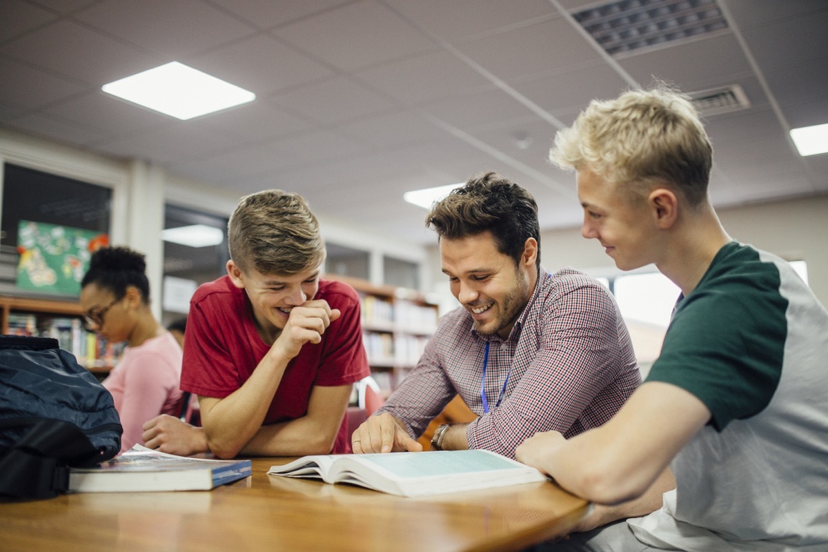 white male teacher laughing with his young students while looking at a book