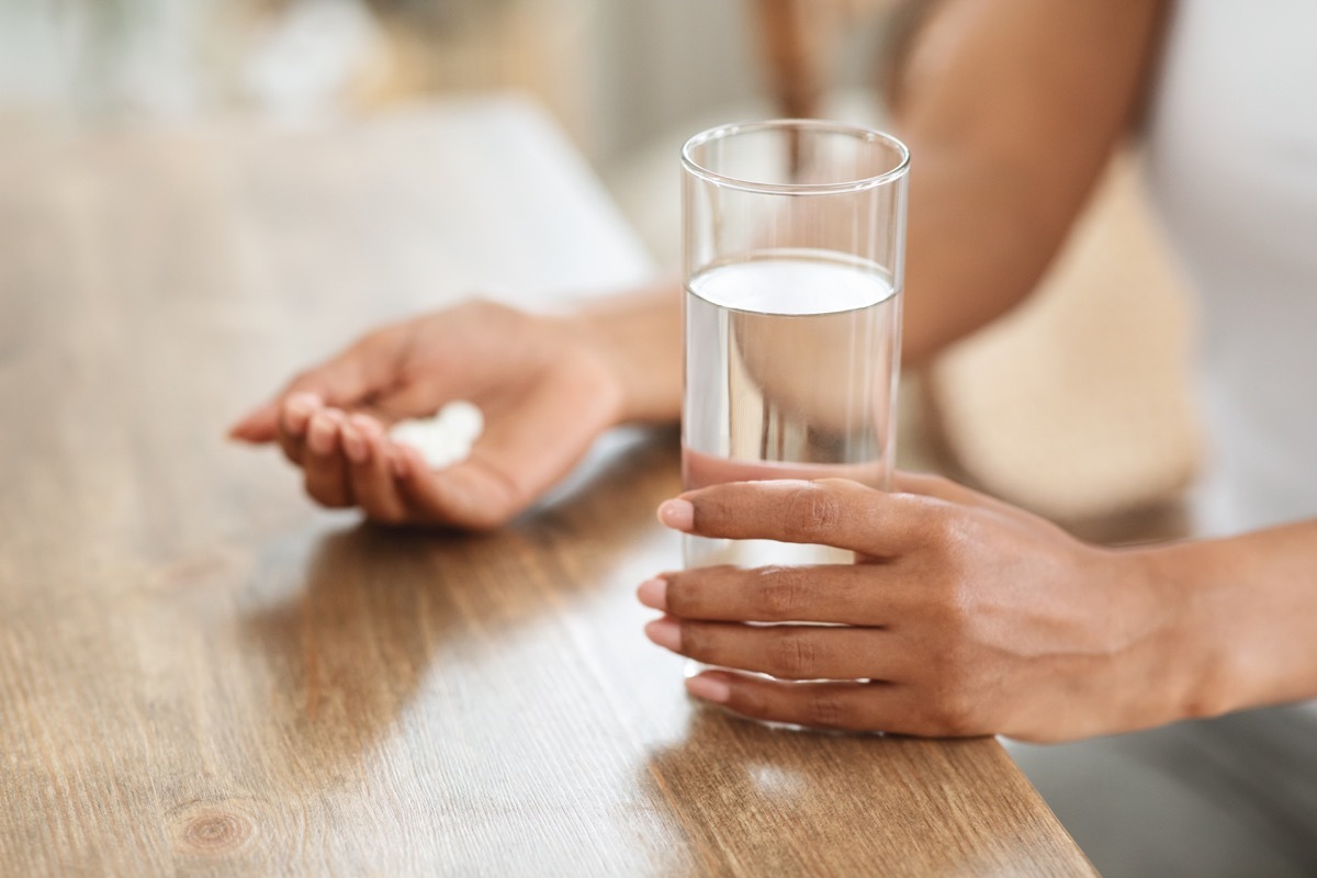 woman takes medicines with glass of water at home, cropped image, closeup