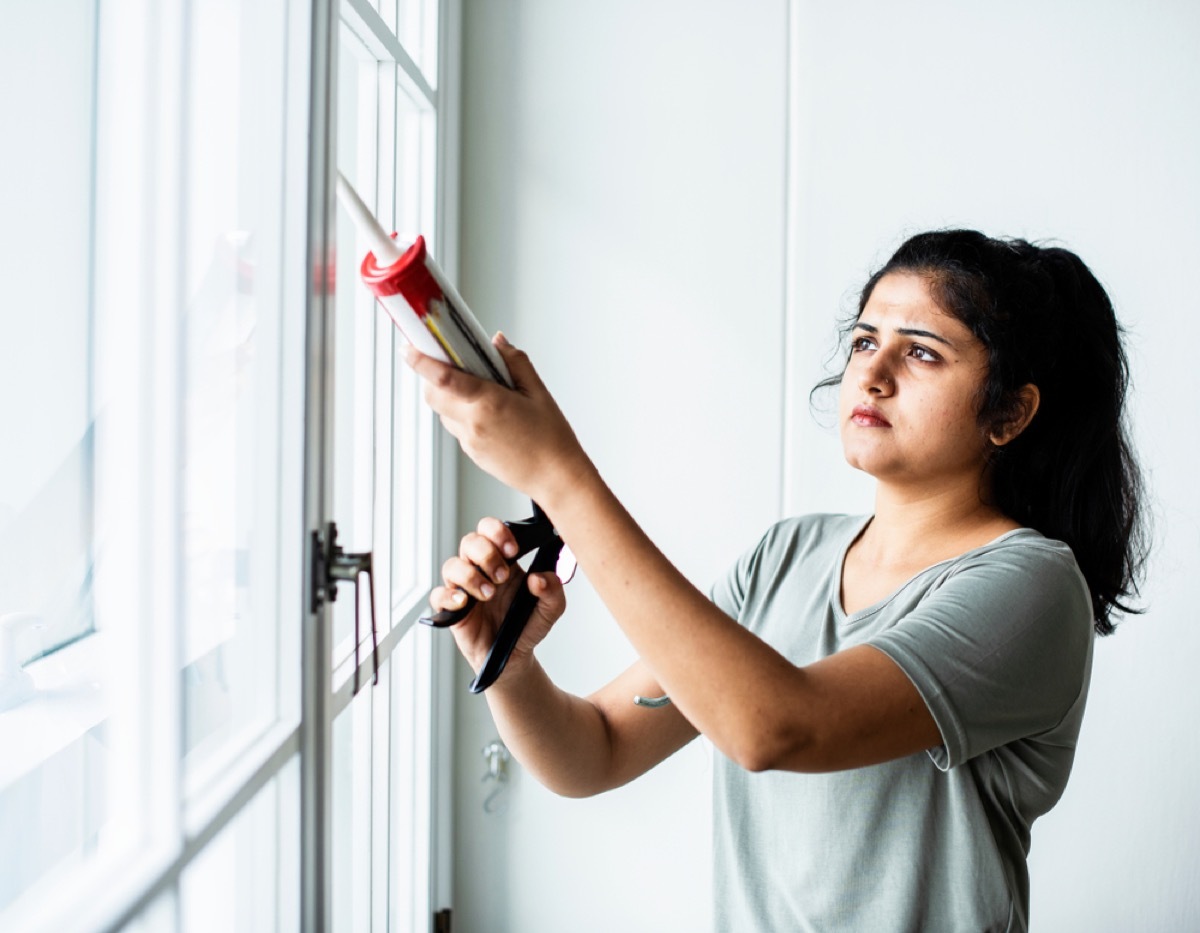 young woman caulks around windows