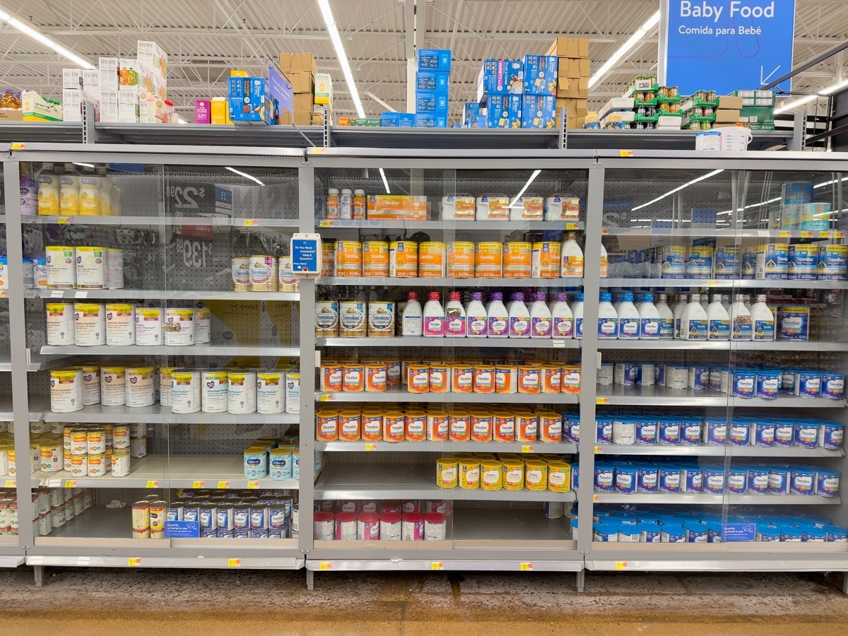 Baby formula behind glass doors on shelves inside a Walmart Supercenter.