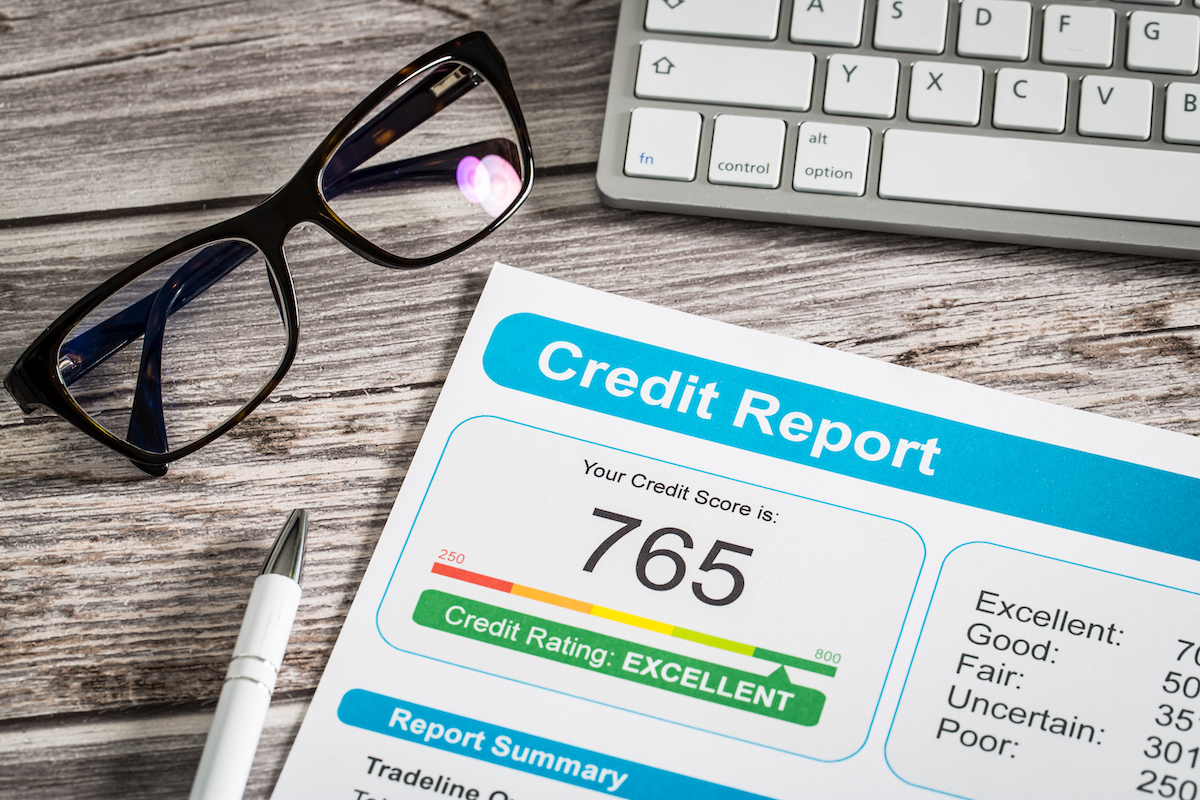 A credit report sitting on a wood desk next to a pen, pair of glasses, and keyboard