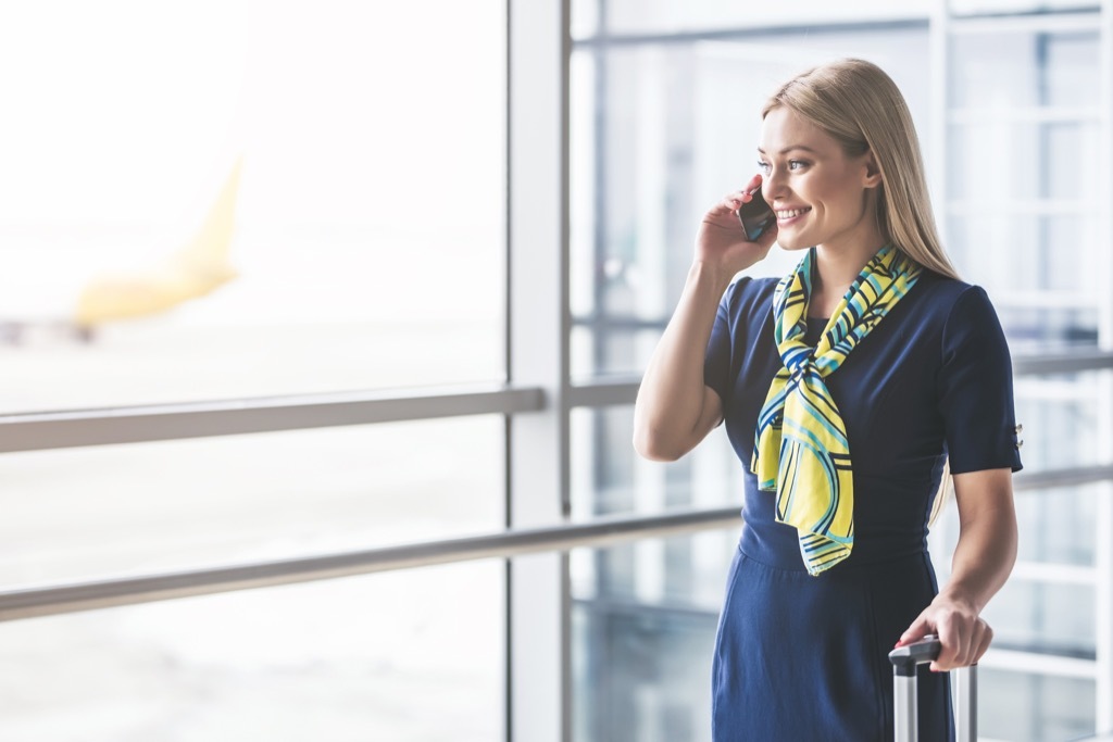 smiling flight attendant in terminal with suitcase