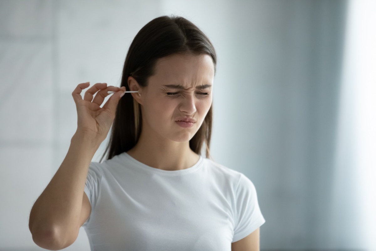 Woman cleaning ears with q-tip uncomfortable