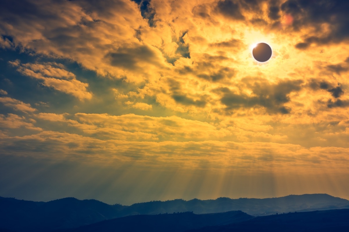 Amazing scientific natural phenomenon. The Moon covering the Sun. Total solar eclipse with diamond ring effect glowing on sky above mountain range. Serenity nature background.