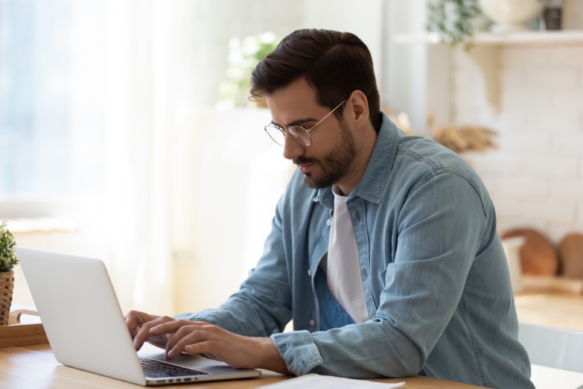 white man sitting and typing on his laptop while leaning forward