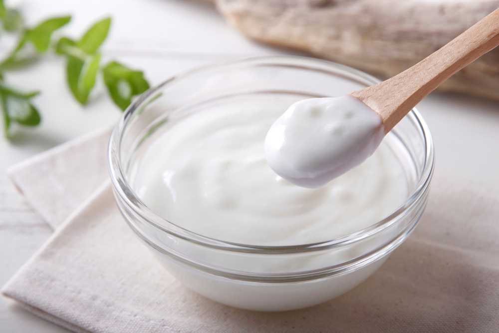 A bowl of fresh yogurt on a table with a wooden spoon