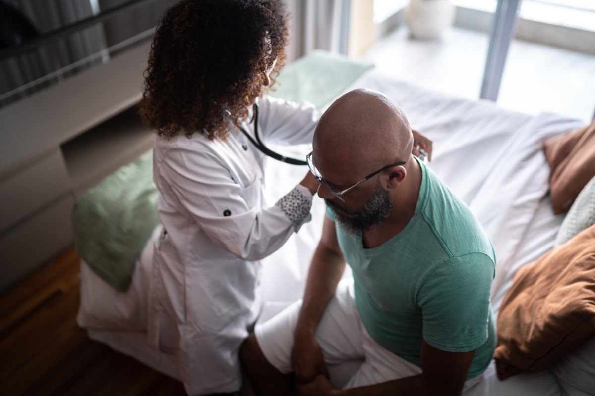 Doctor listening to patient's heartbeat during home visit