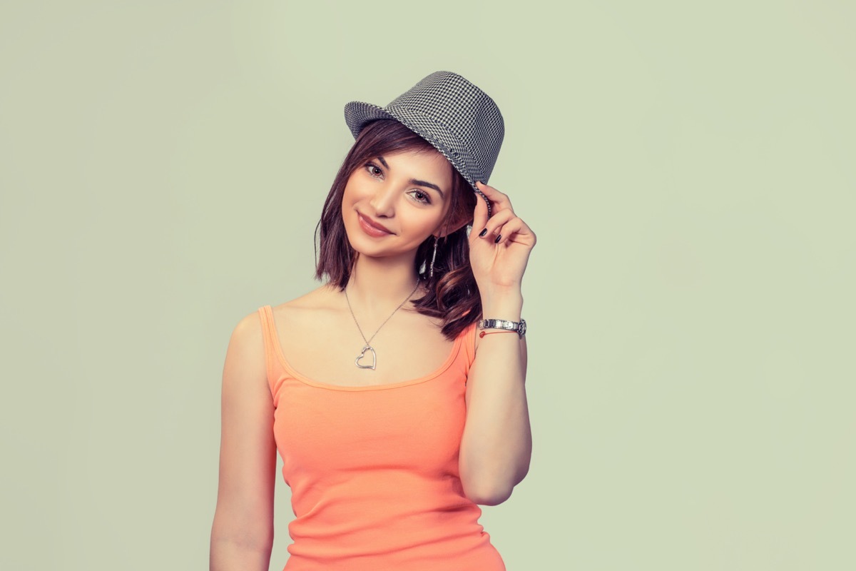 Woman touching her gray hat in sign of salute, greeting someone saying hi with hand gesture