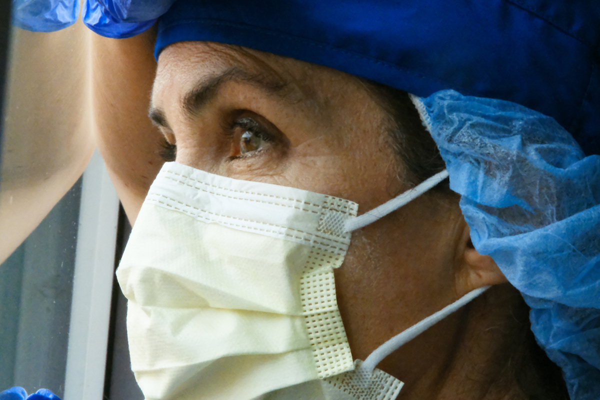 Overworked woman health care worker looking through a window while wearing a mask