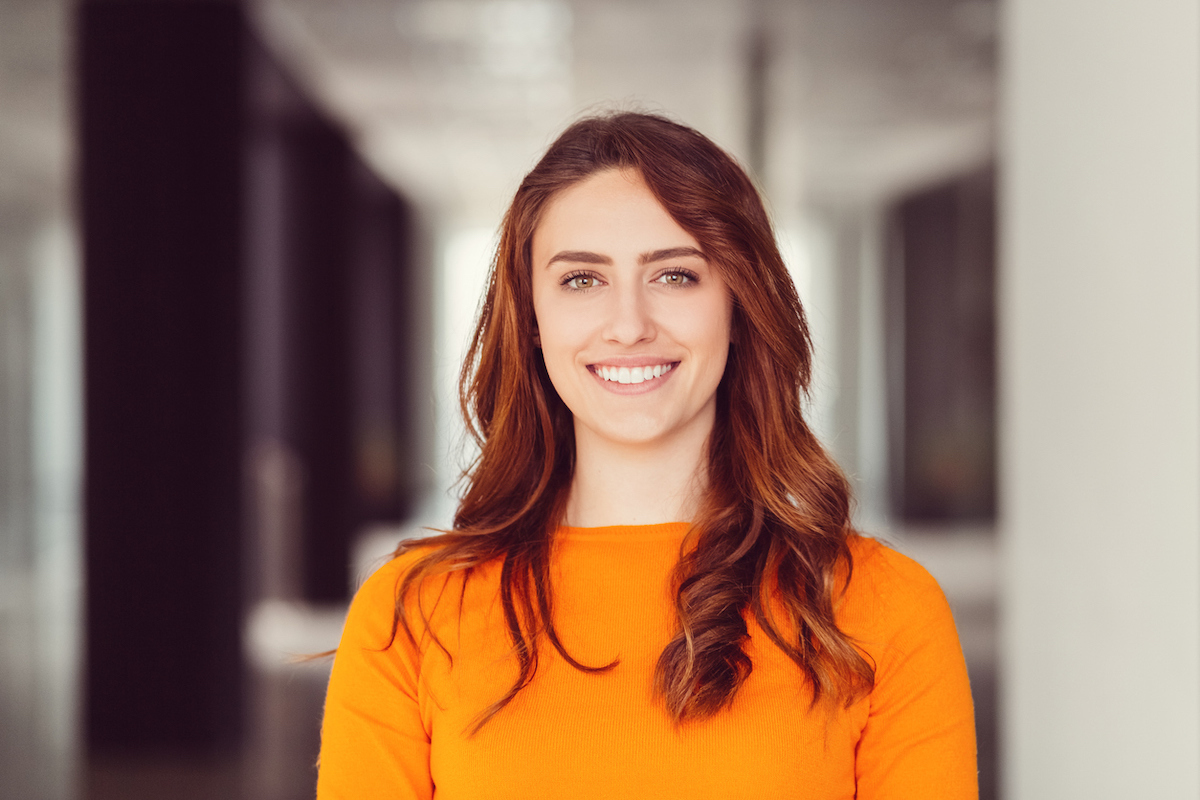 Portrait of a young smiling woman with auburn hair wearing a bright orange sweater