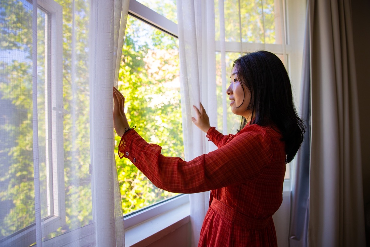 Woman opening window curtains enjoying good morning