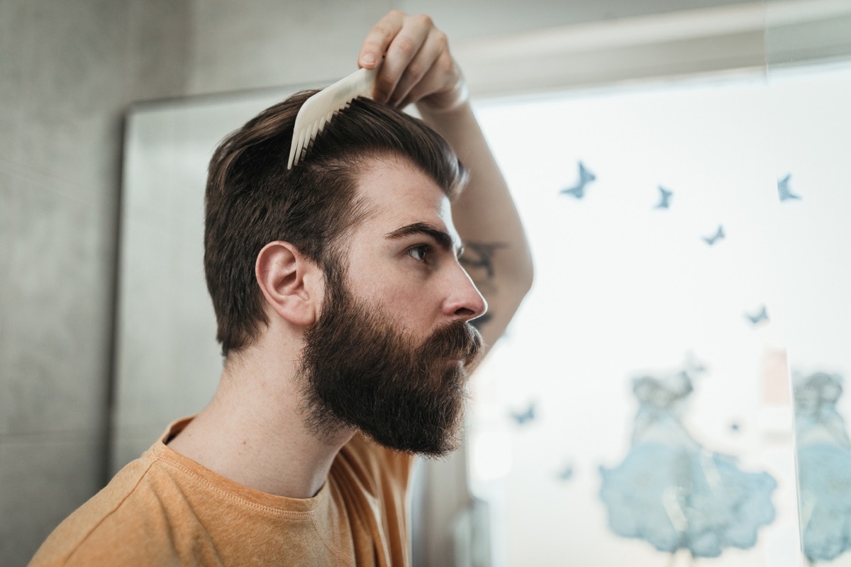 Young handsome man combing hair in the bathroom