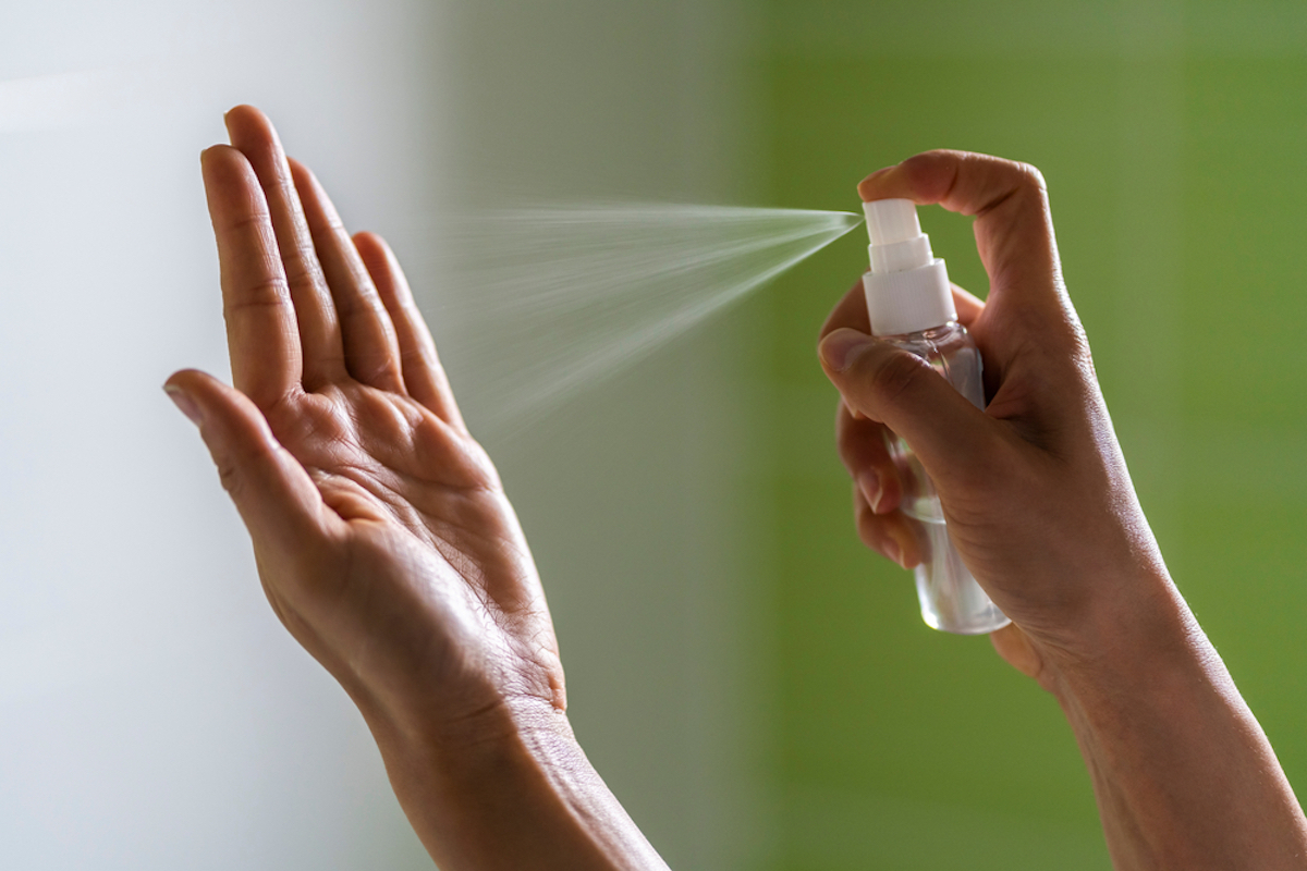 woman's hand sprays from spray bottle onto other hand