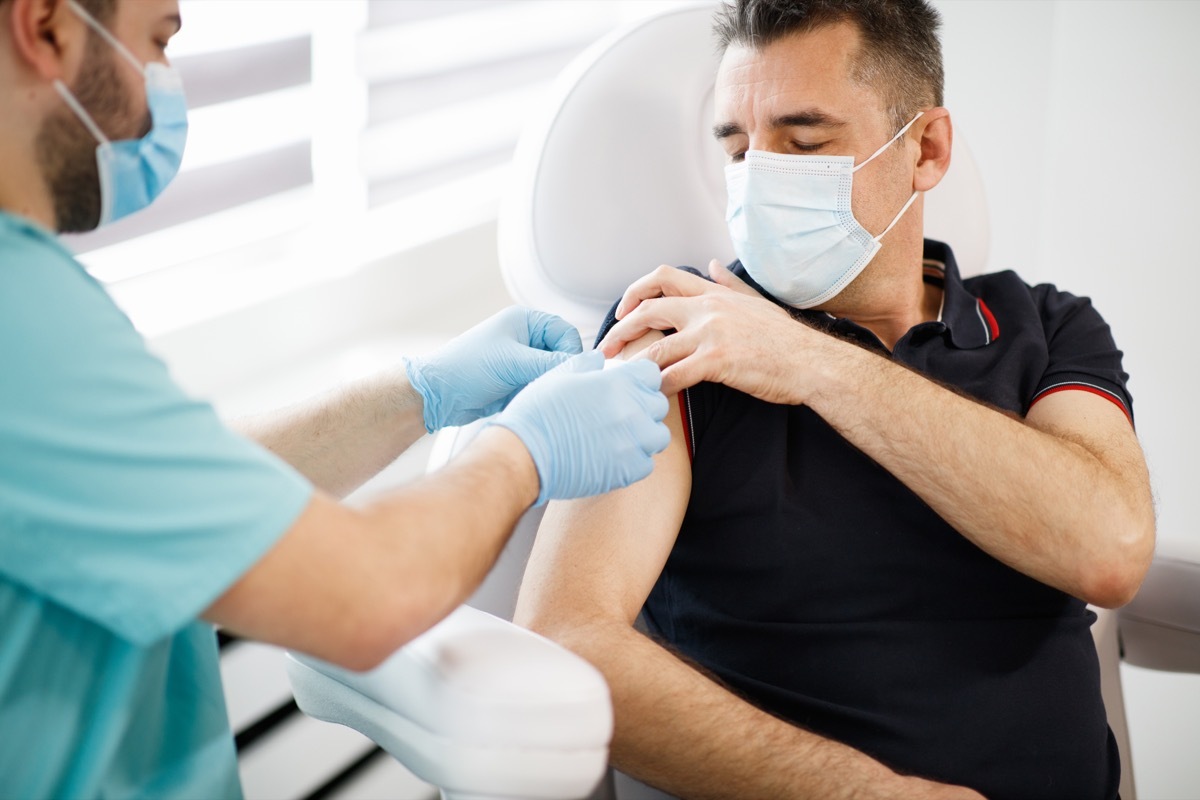 Doctor and patient wearing protective face masks due to COVID-19 pandemic, disinfection and securing with adhesive tape after vaccination