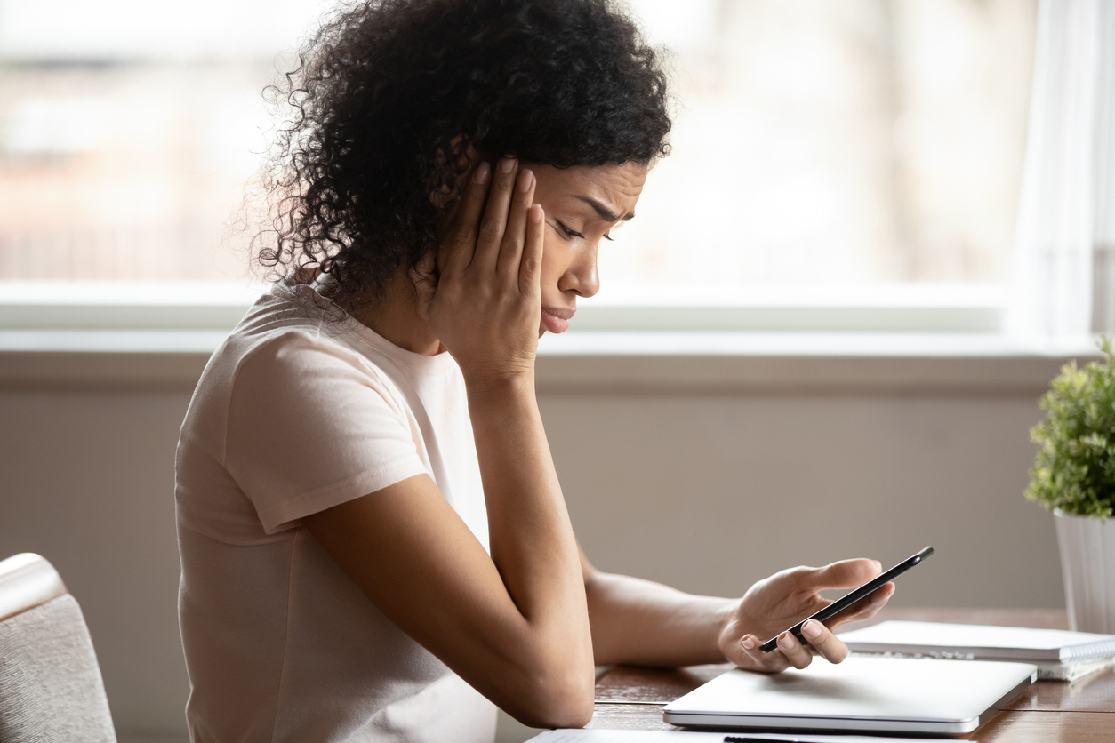 A young woman looks at text message on her smartphone with a worried expression on her face.