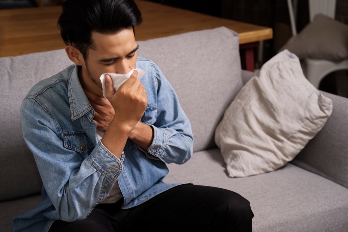 young man in denim shirt coughing into tissue