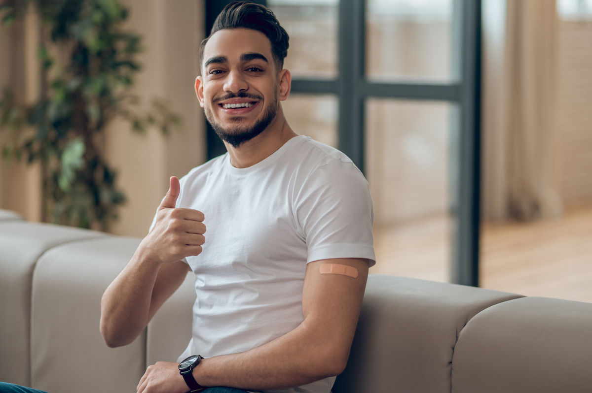 Young man wearing a white t-shirt sitting on his couch giving a thumbs up.