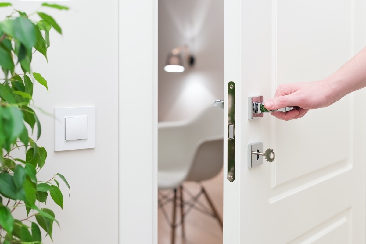 Modern white door with chrome metal handle and a man's arm.