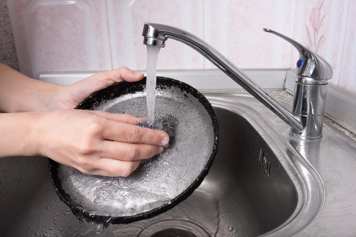 white hand scrubbing pan with steel wool