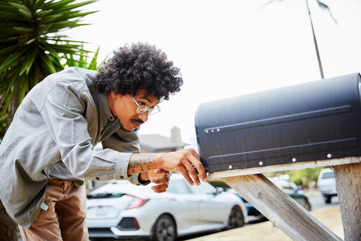 man looking into mailbox in street