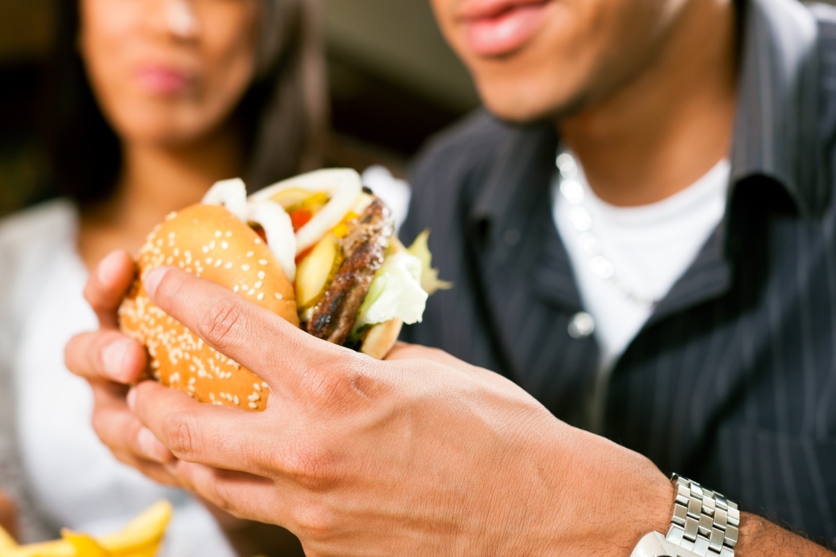 man eating burger while woman watches