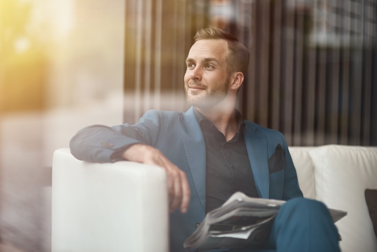 Overconfident Business Man wearing a blue suit sitting on a white couch