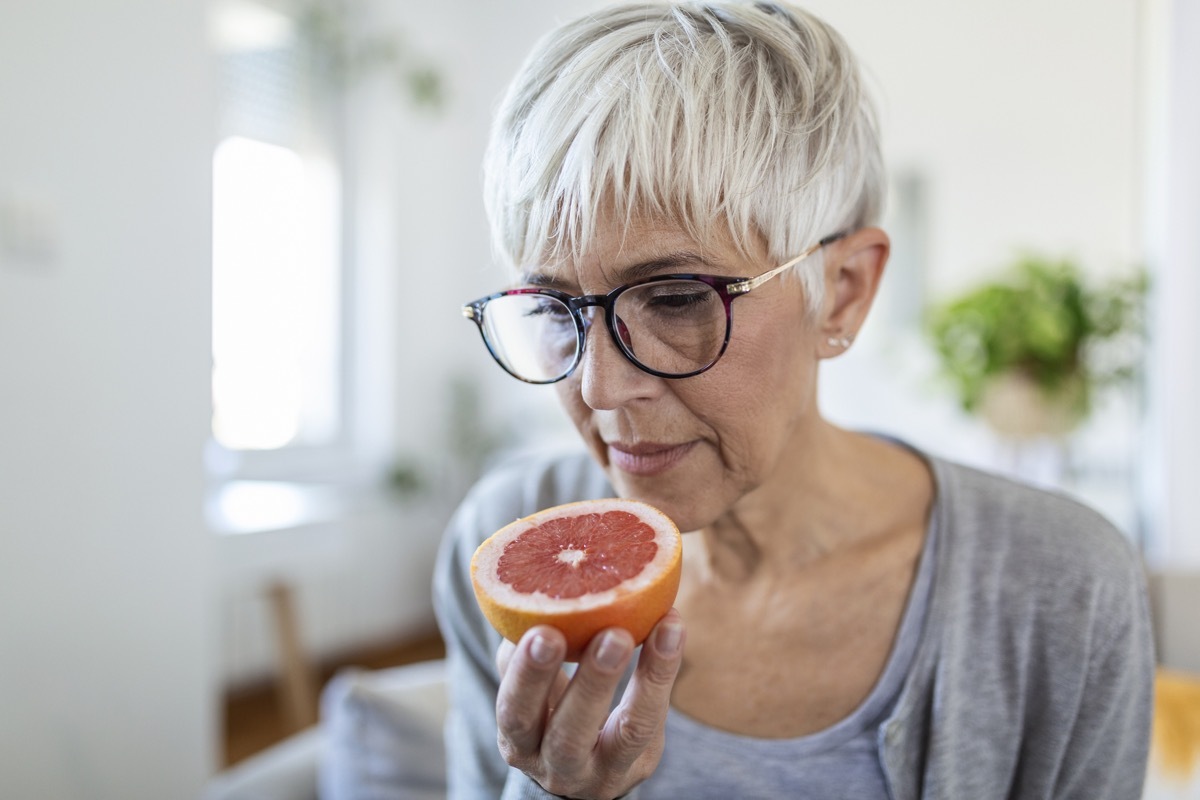 Sick woman trying to sense smell of half fresh orange, has symptoms of Covid-19, corona virus infection - loss of smell and taste. One of the main signs of the disease.