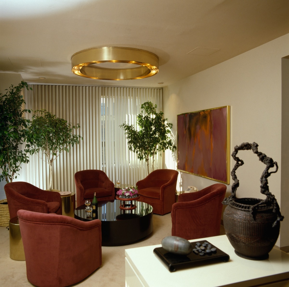 A9K1RP Circular metal light fitting in eighties livingroom with red velour sofas and vertical Venetian blinds