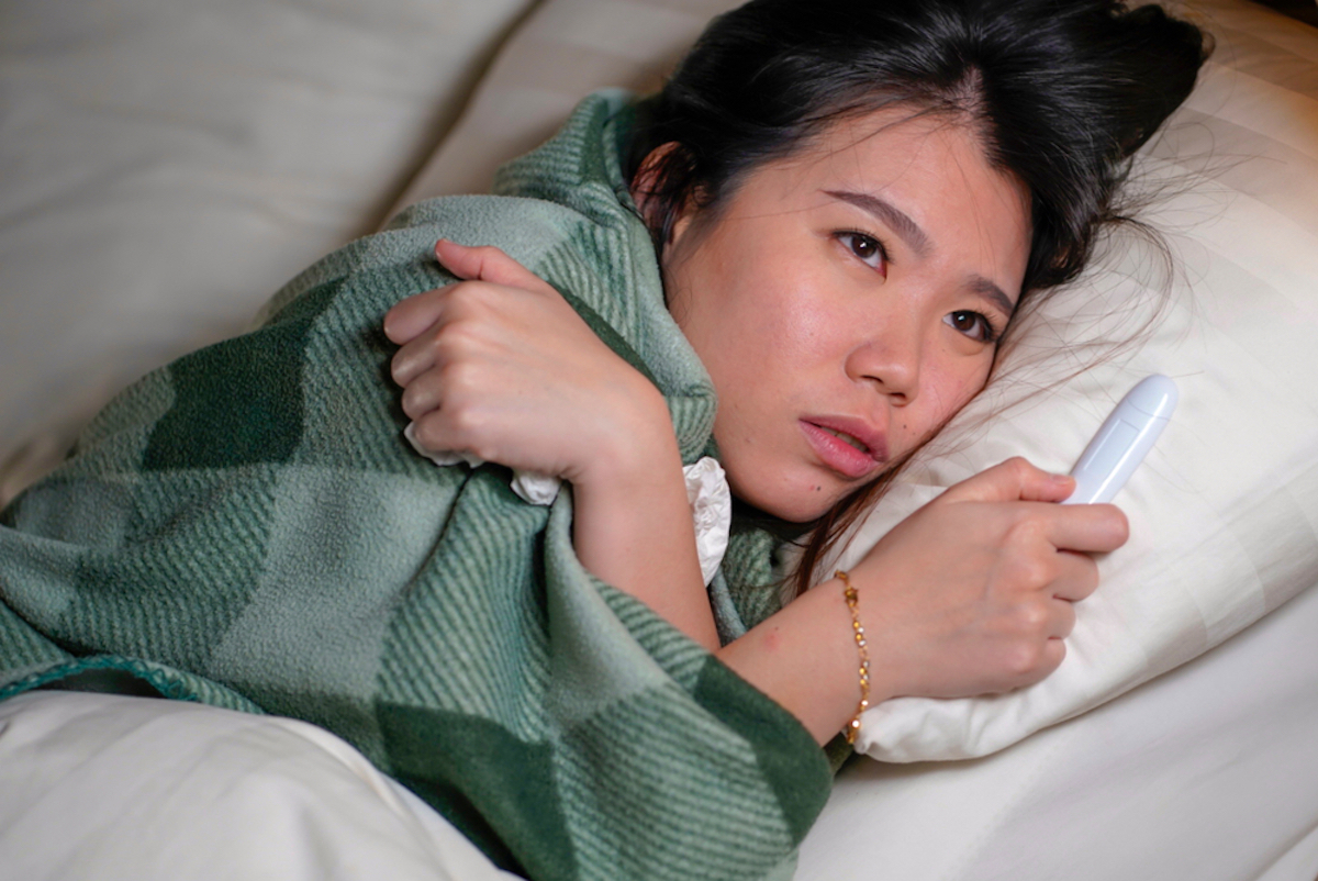 Woman home sick with fever covered in blanket