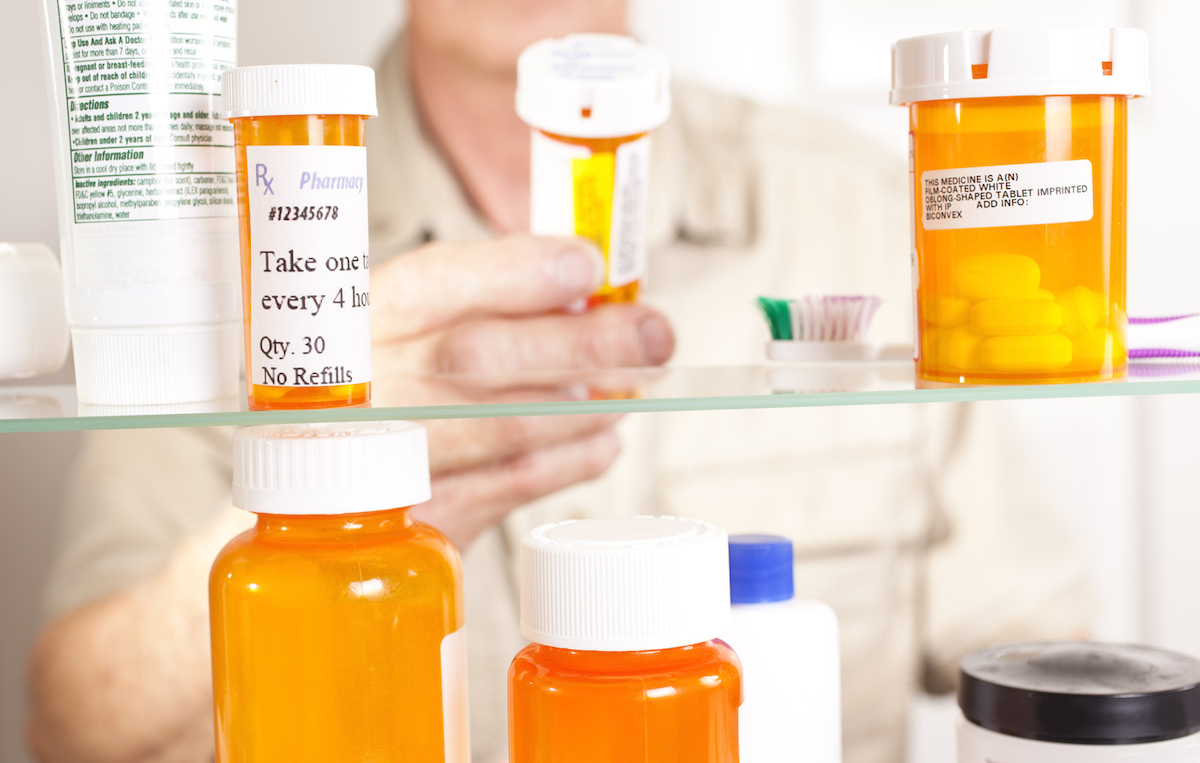 Senior adult man gets prescription medicines out of his medicine cabinet. Close up of hands and pills.