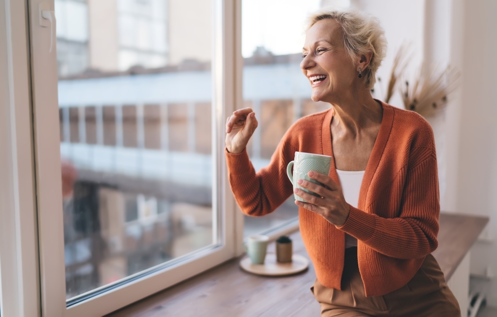 Stylish senior woman laughing wearing orange cardigan with coffee mug