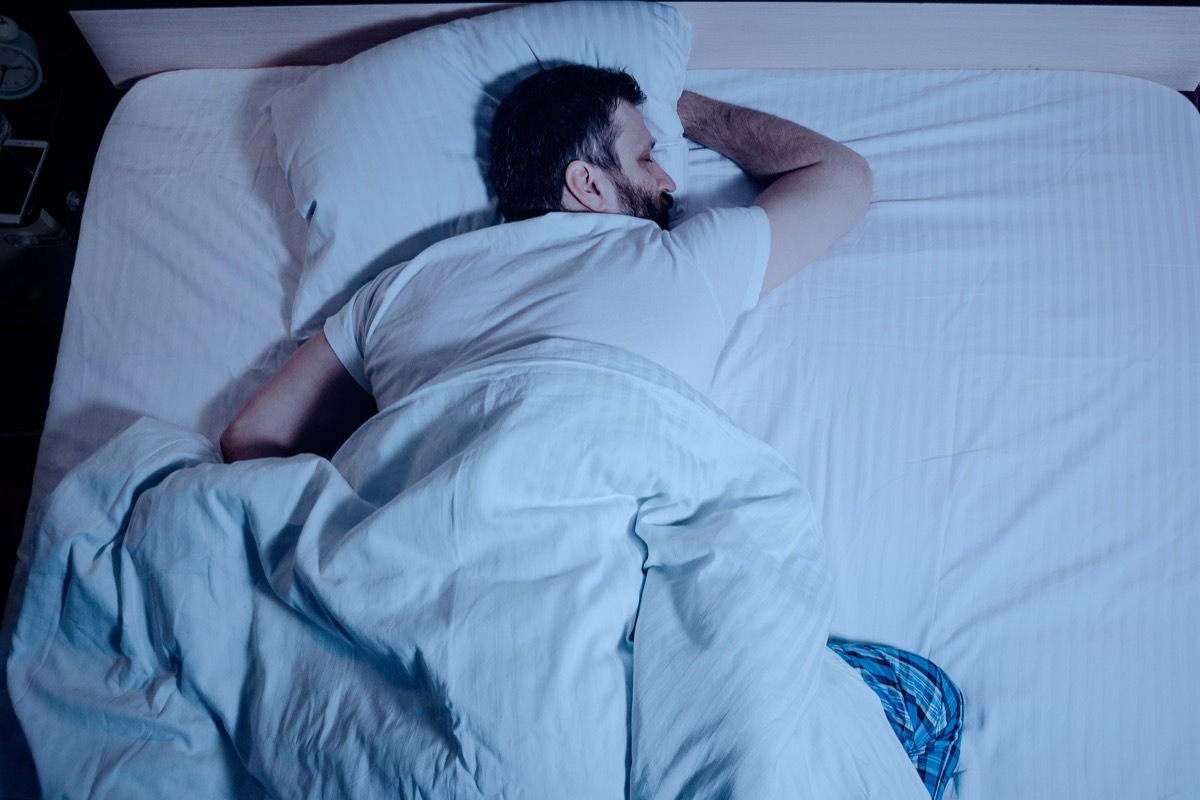 dark haired man sleeping on his stomach in bed