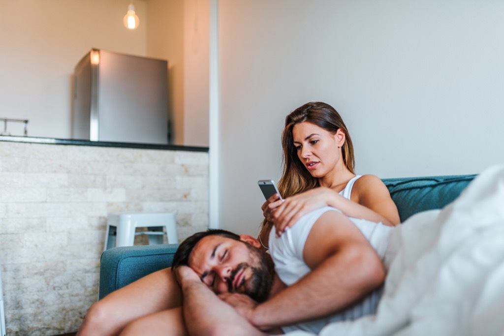 Girlfriend checking her boyfriend's phone while he sleeps