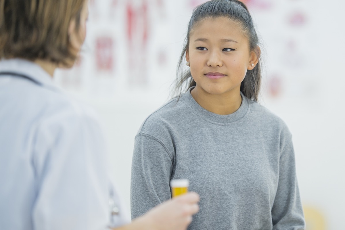  girl is indoors in a physiotherapy clinic. She is wearing casual clothing. A female doctor wearing a lab coat is giving her medication for her injury.