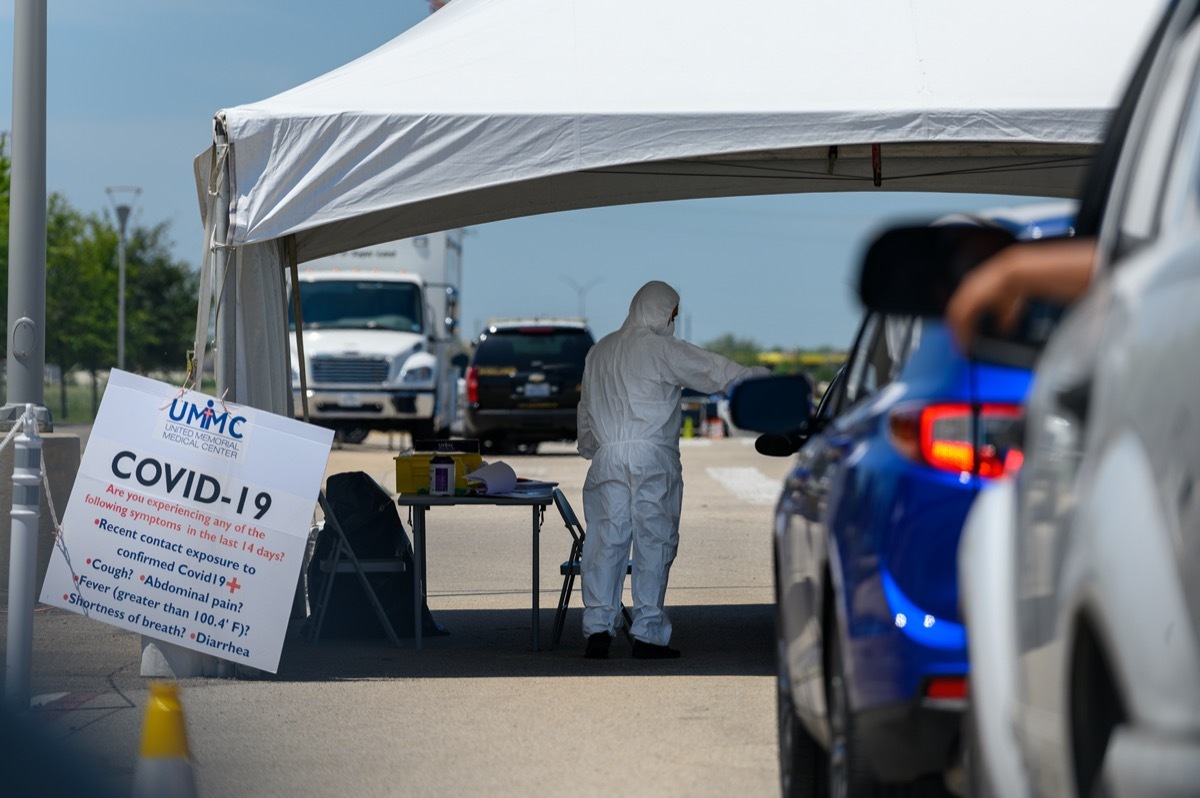 Dressed in full protective gear a healthcare worker collects information from people sitting inside their car at the COVID-19 drive-through testing site.