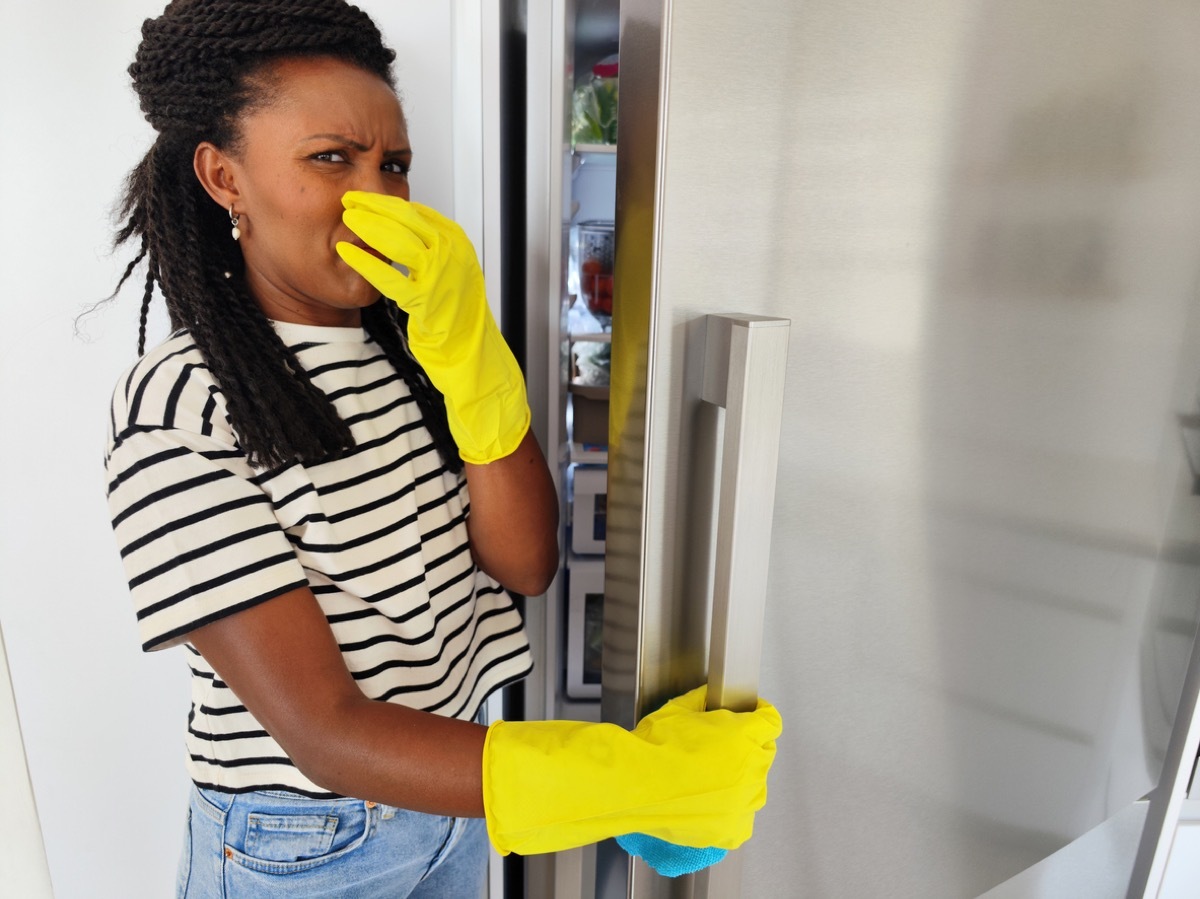 woman opening door and feeling a bad smell from the refrigerator in kitchen.