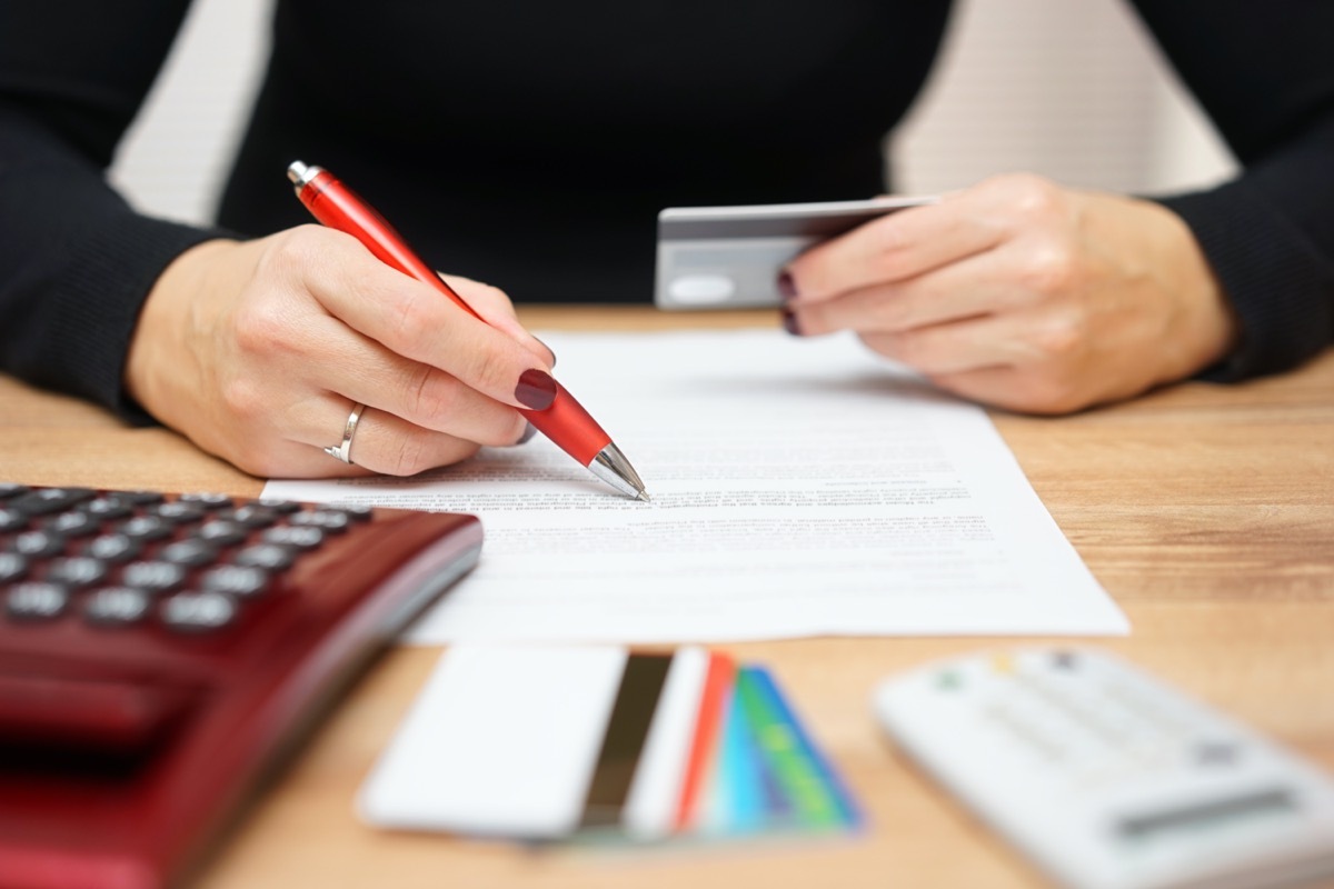 woman's hand holding over a bill and a credit card in her other hand, while in front of other cards and a calculator