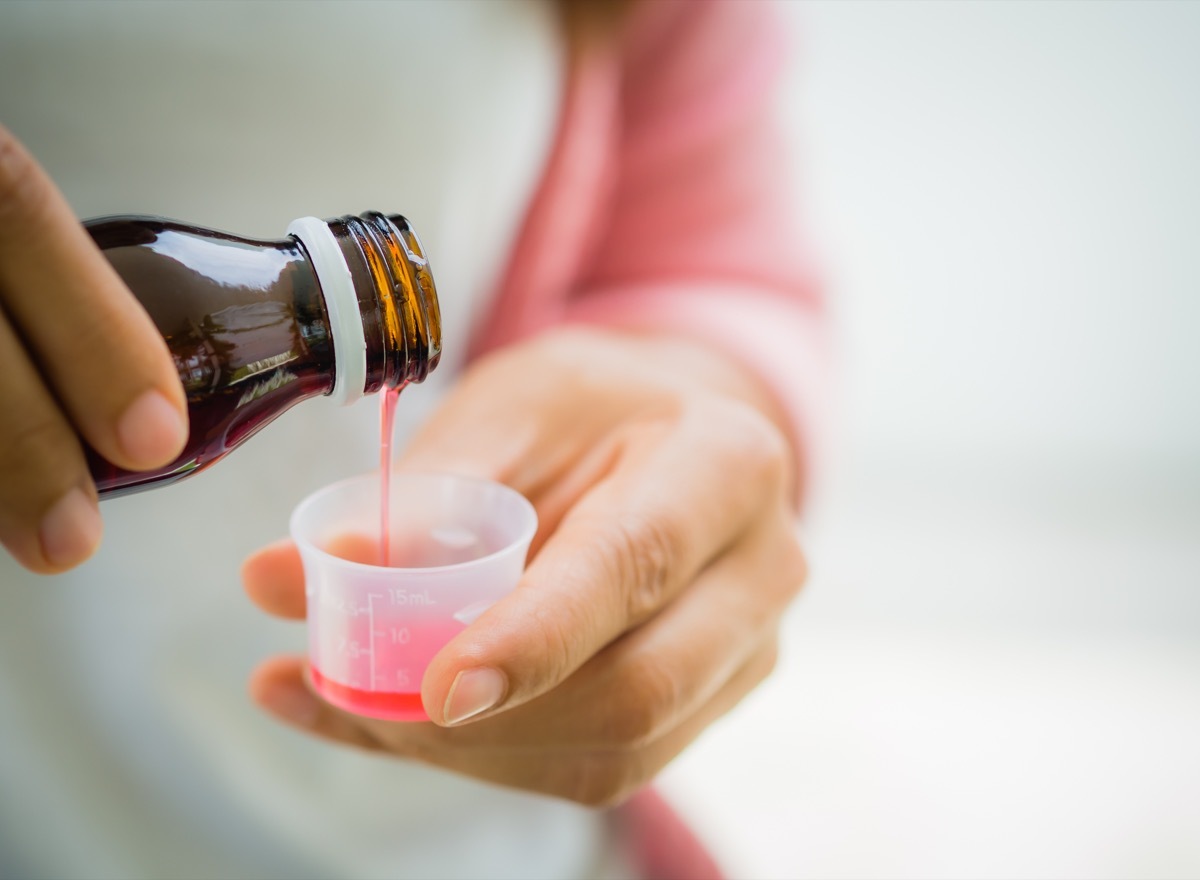 Closeup woman pouring medication or antipyretic syrup from bottle to cup. Healthcare, people and medicine concept -