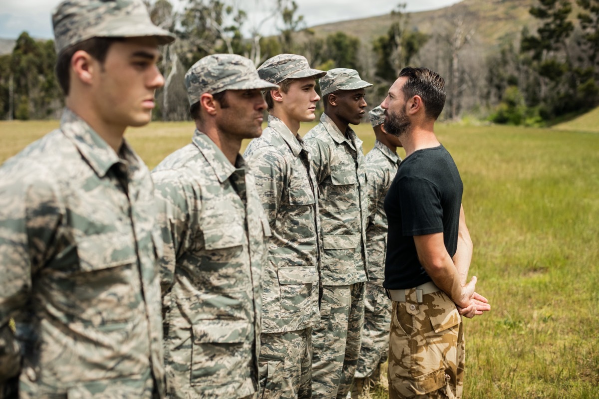 five military men standing in a line and a military officer looking at one of them in the eye during combat training