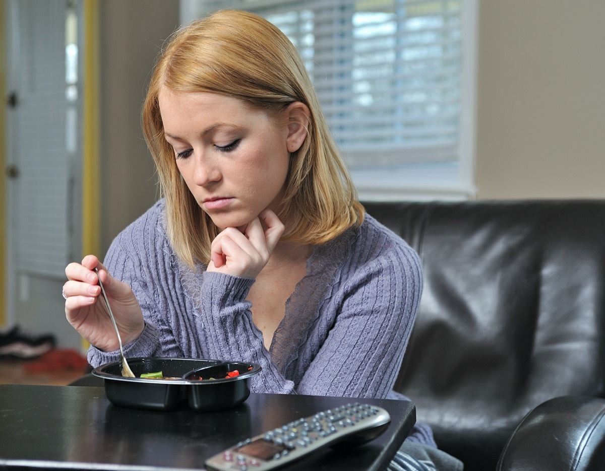 woman sitting in chair in pastel sweater eating a frozen (TV) dinner