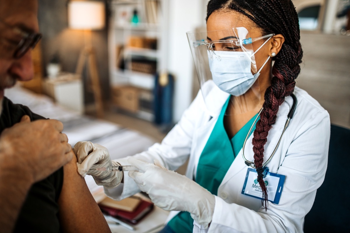 Mid adult female doctor at home visit giving a vaccine to a senior patient