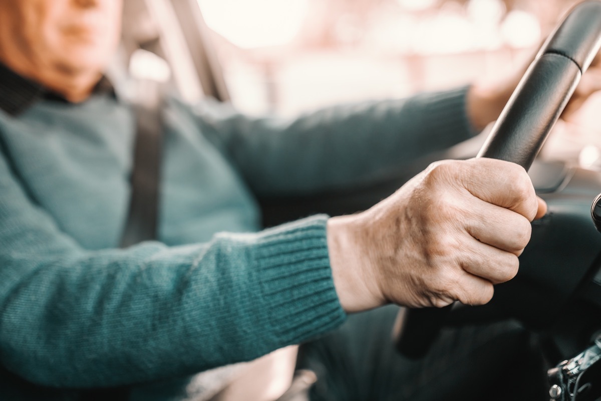 Close up of senior man holding hands on steering while and driving his car.