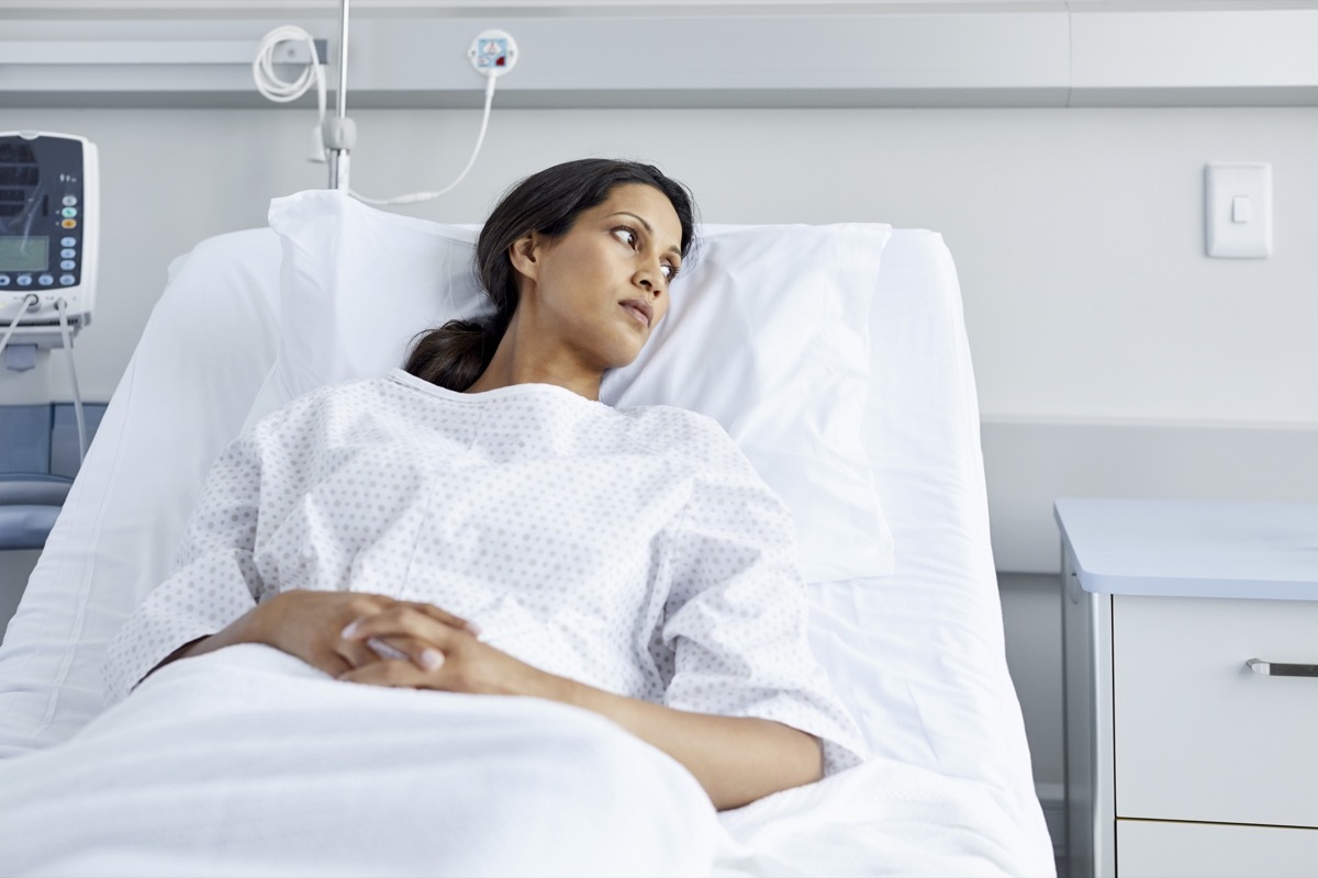 Thoughtful patient lying on bed. Female is wearing hospital gown. She is looking away.