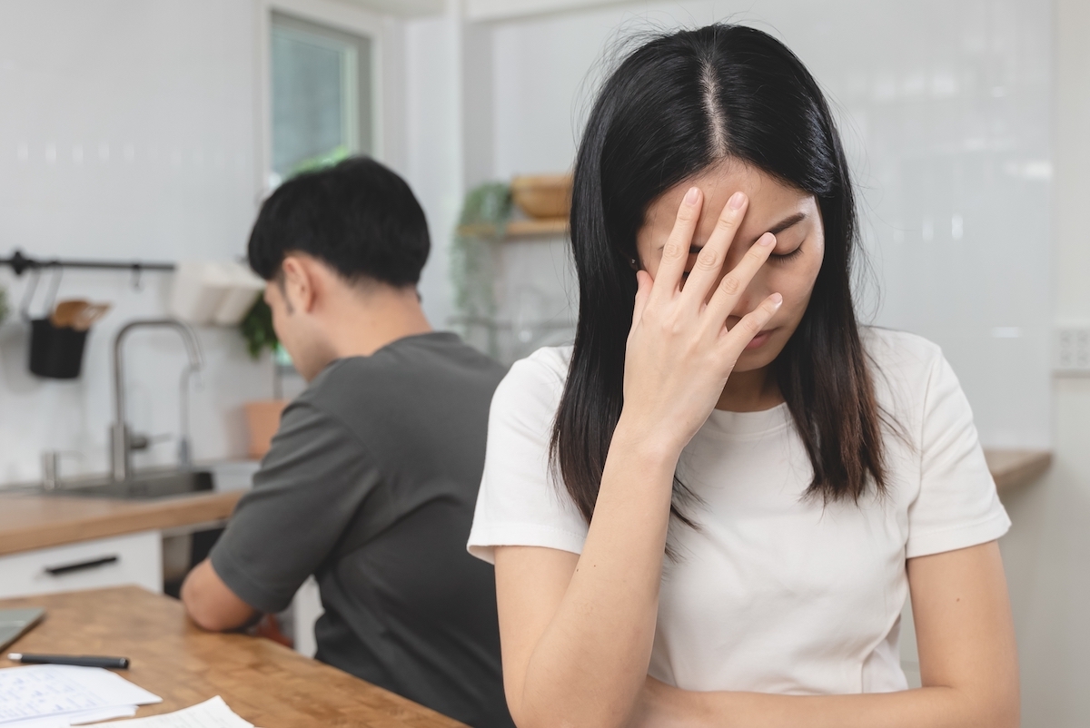 A young couple turned away from each other in the kitchen, with the female looking distressed.