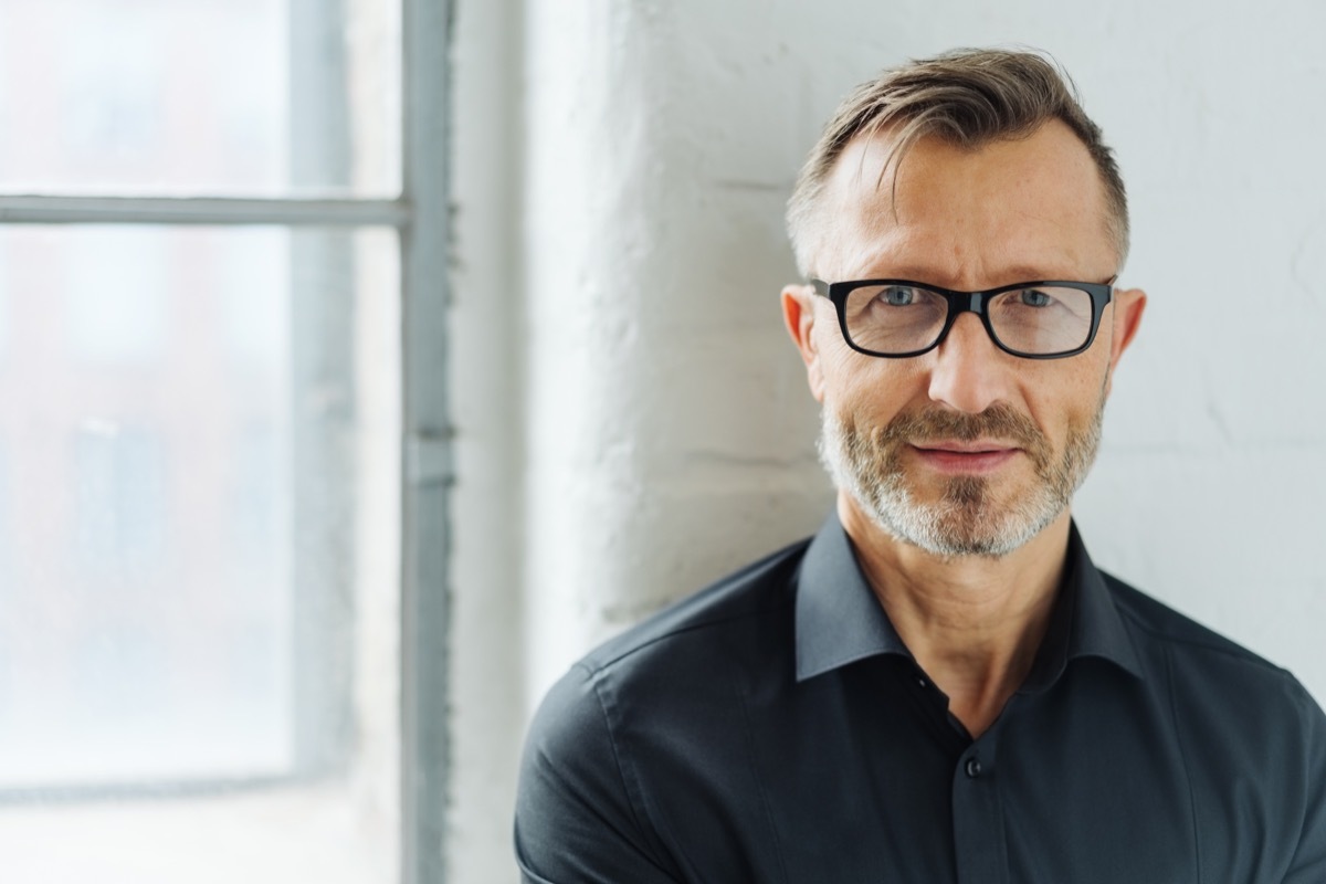 Bearded middle-aged man wearing glasses looking at camera with a serious expression in a close up head and shoulders portrait