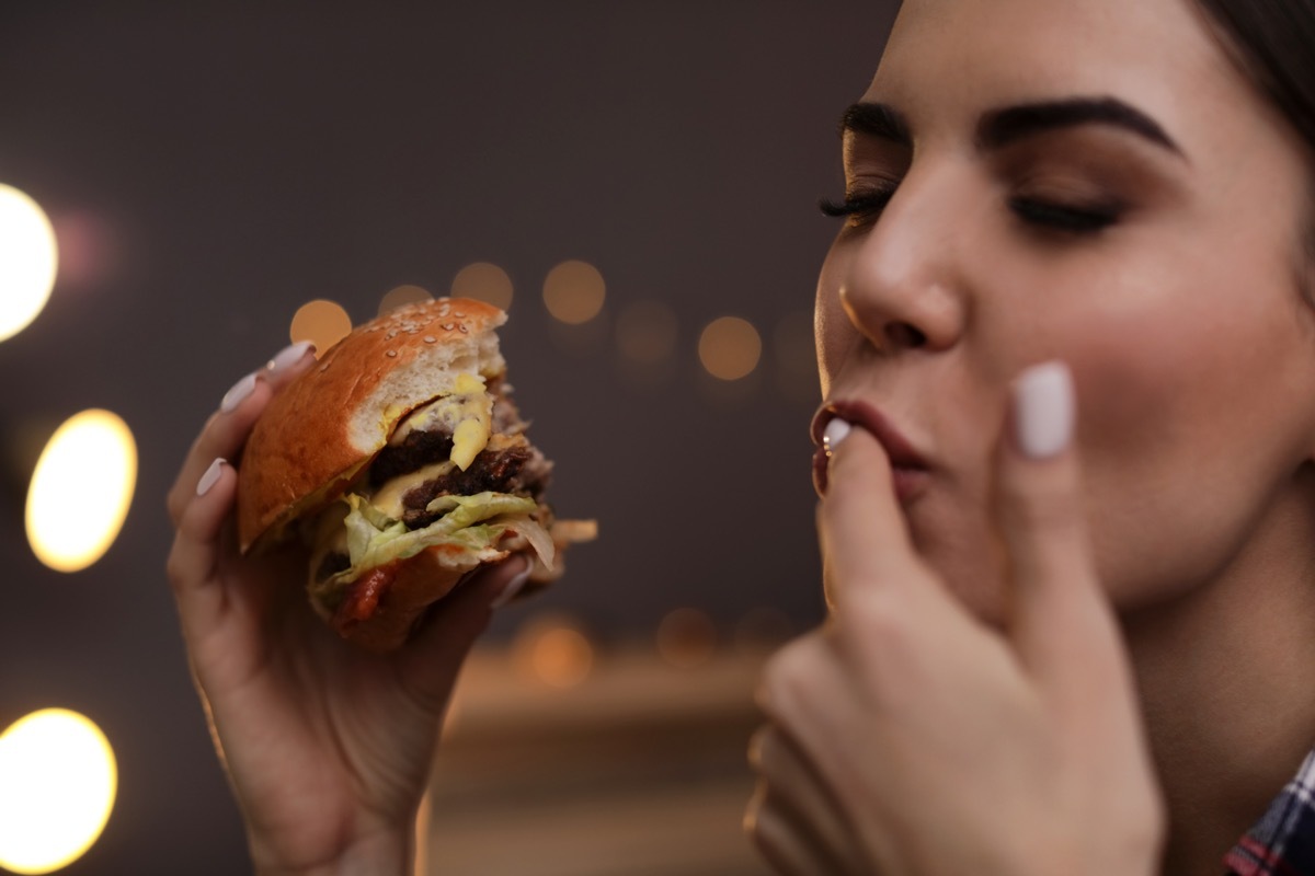 Woman Licking Her Fingers While Enjoying a Burger BBQ Etiquette Mistakes