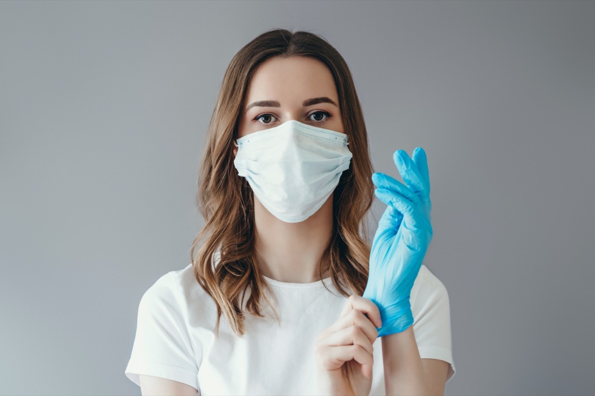 woman patient in a medical mask puts on protective surgical sterile gloves on her arm