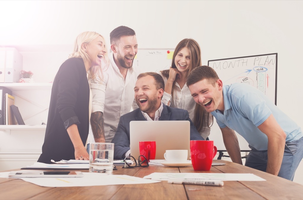 coworkers gathered around a laptop laughing